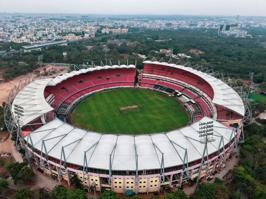 An aerial view of Lords Cricket Ground showing the oval-shaped pitch area in the center, surrounded by a green outfield with well-maintained grass. The seating stands are visible along the perimeter i